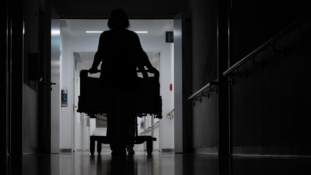 Foto: Eine Krankenpflegerin schiebt ein Krankenbett durch den Gang einer Station.