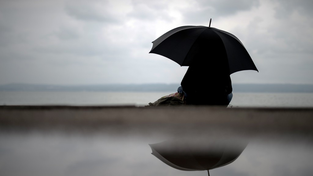 Eine Frau sitzt bei verregnetem Wetter unter einem Regenschirm