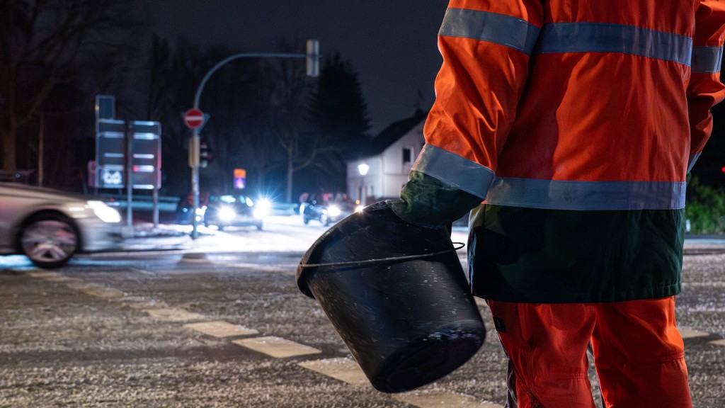 Ein Mitarbeiter des Winterdienstes wartet mit einem Eimer vor einer Kreuzung.