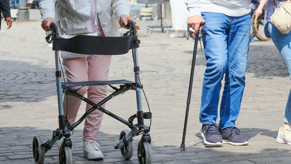 Foto:Zwei Senioren mit Rollator und Gehstock in einer Fußgängerzone
