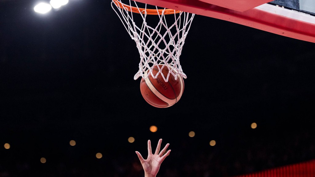 Hände einer Basketballspielerin am Ball vor dem Korb