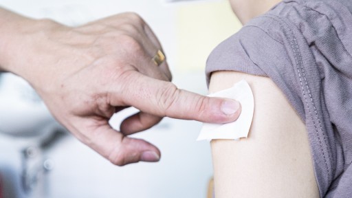 Ein Kinder- und Jugendarzt drückt einen Tupfer an die Impf-Stelle am Arm einer jungen Frau. 